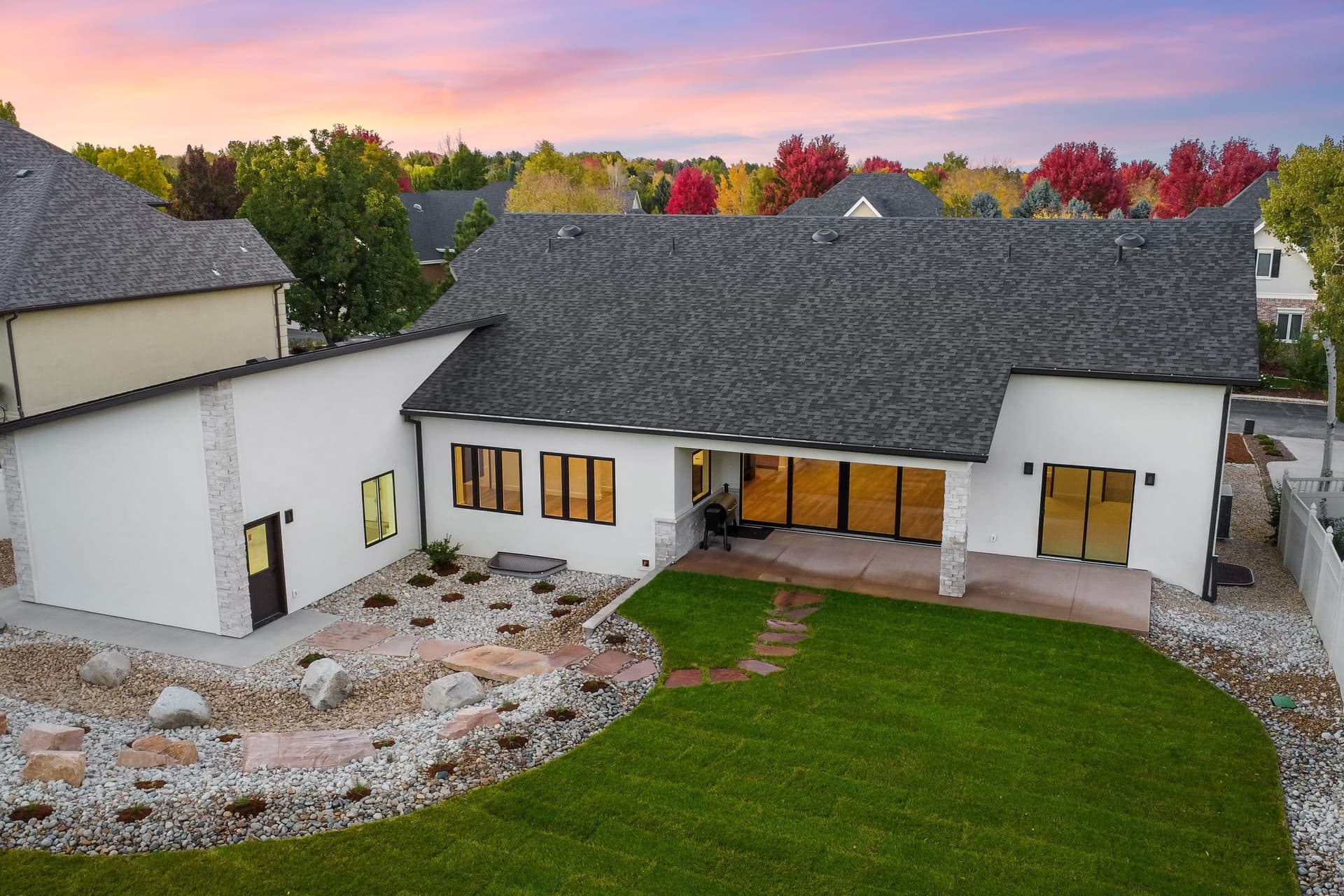 Rear aerial at twilight — backyard landscaping, covered patio, and fall foliage surrounding the property