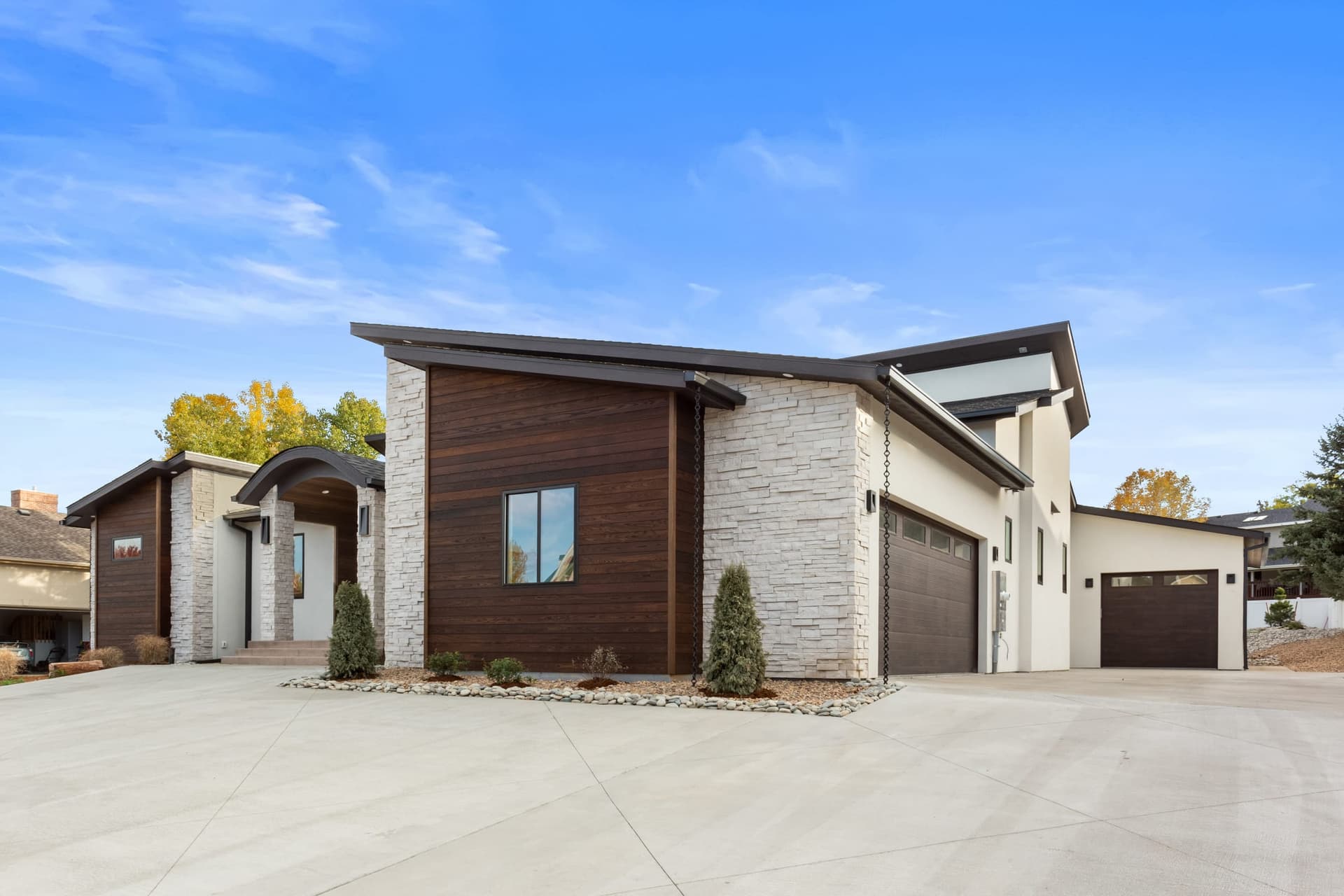 Garage wing with dark wood-tone flush-panel doors, stucco and ledgestone accents, concrete motor court