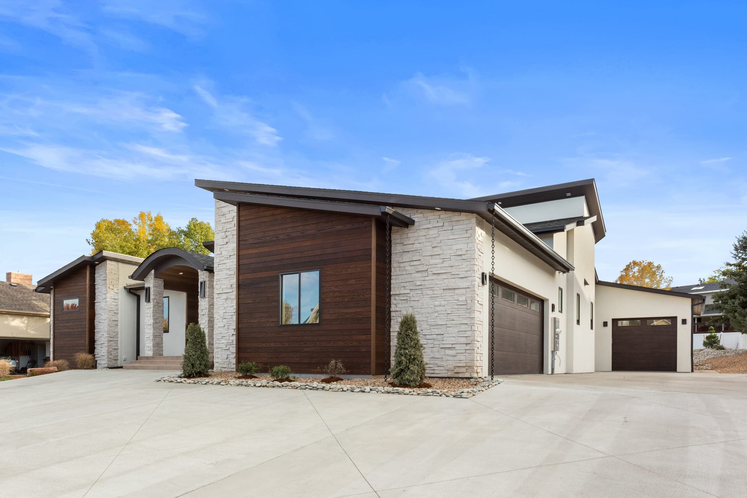 Garage wing with dark wood-tone flush-panel doors, stucco and ledgestone accents, concrete motor court