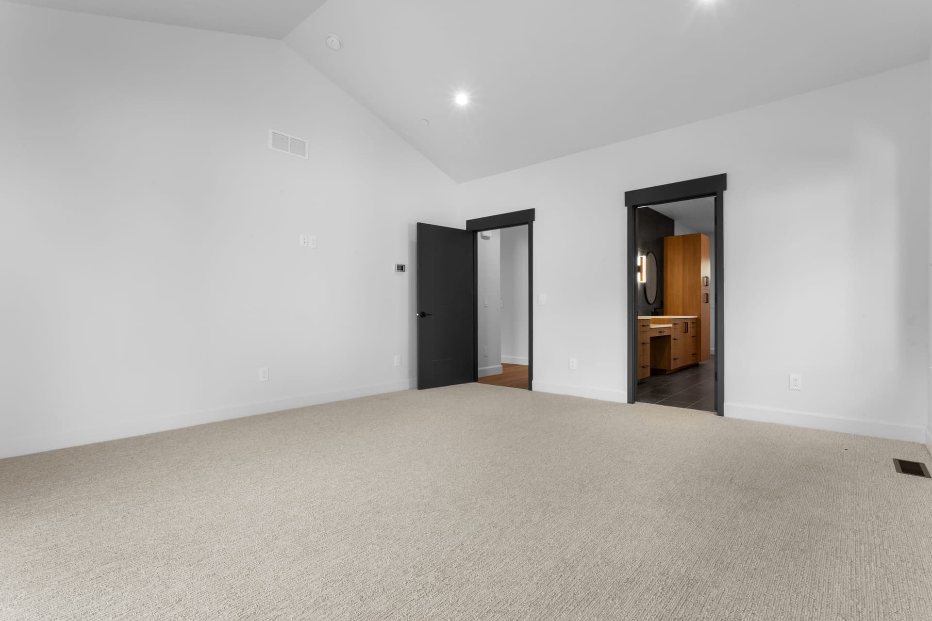 Primary bedroom toward ensuite and walk-in closet — black-framed doors, vaulted ceiling