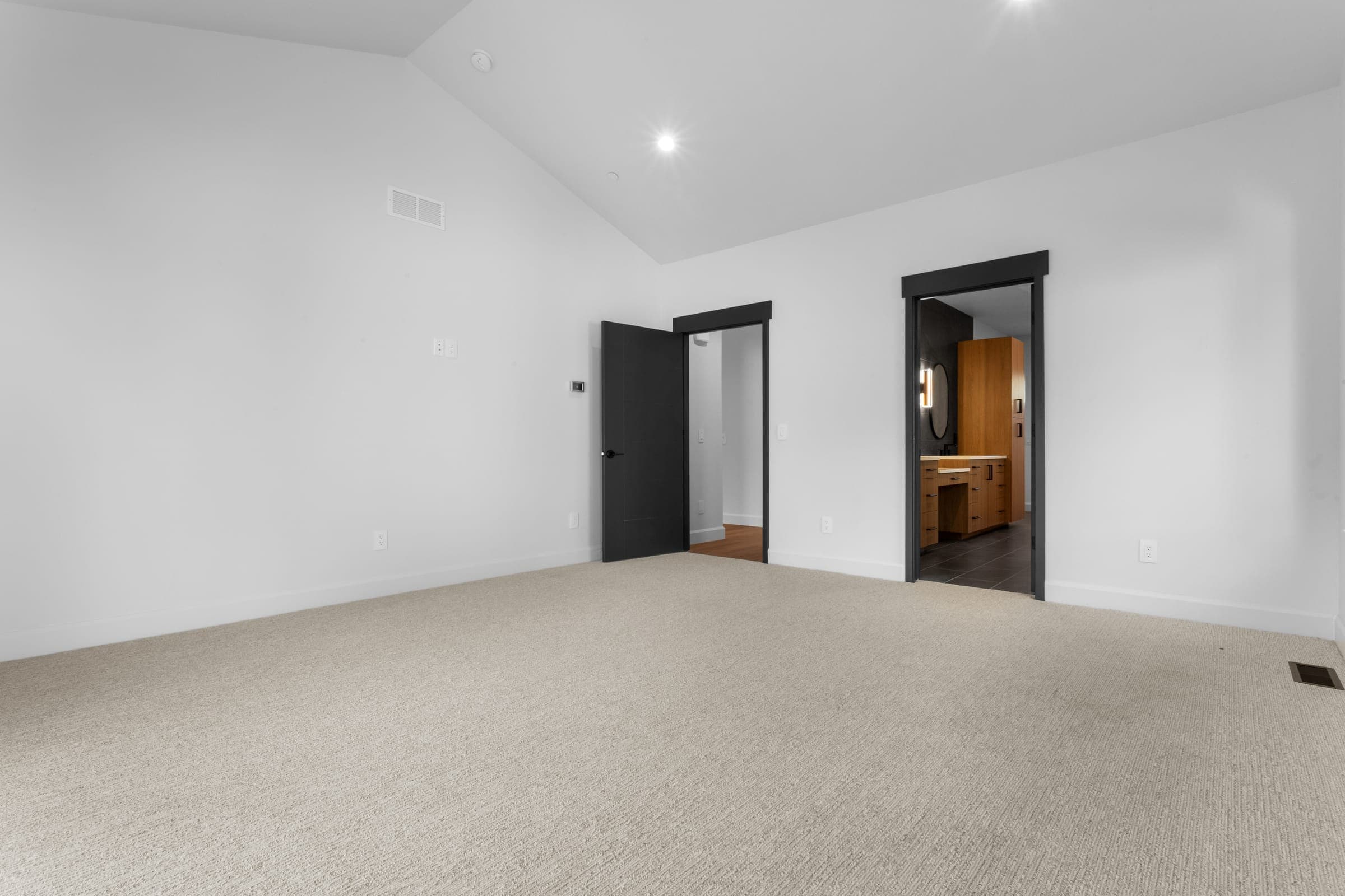Primary bedroom toward ensuite and walk-in closet — black-framed doors, vaulted ceiling