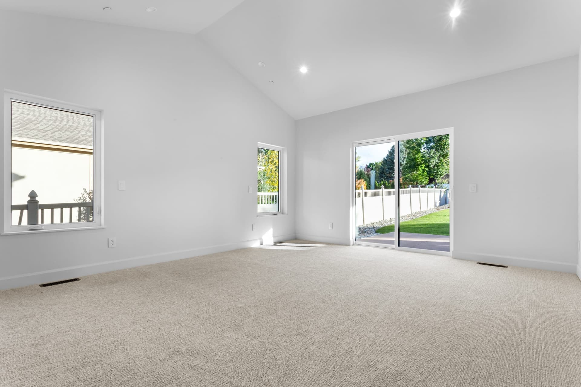 Primary bedroom — vaulted cathedral ceiling, wall of windows, sliding glass patio door to backyard, neutral plush carpet